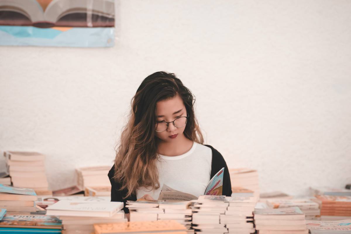 College student holding stack of textbooks next to savings tracker showing college textbook savings progress